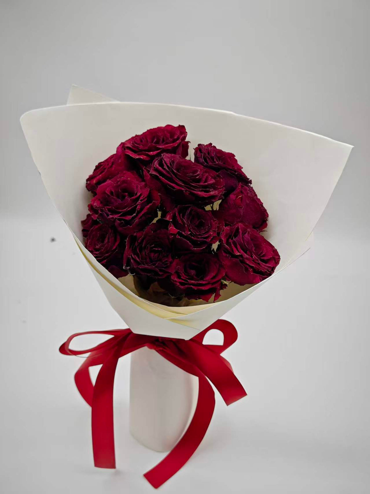 Velvet Rougeの制作例。白い包装紙と赤いリボンで束ねた、花の高さに自然な差がある赤いバラのドライフラワーブーケ